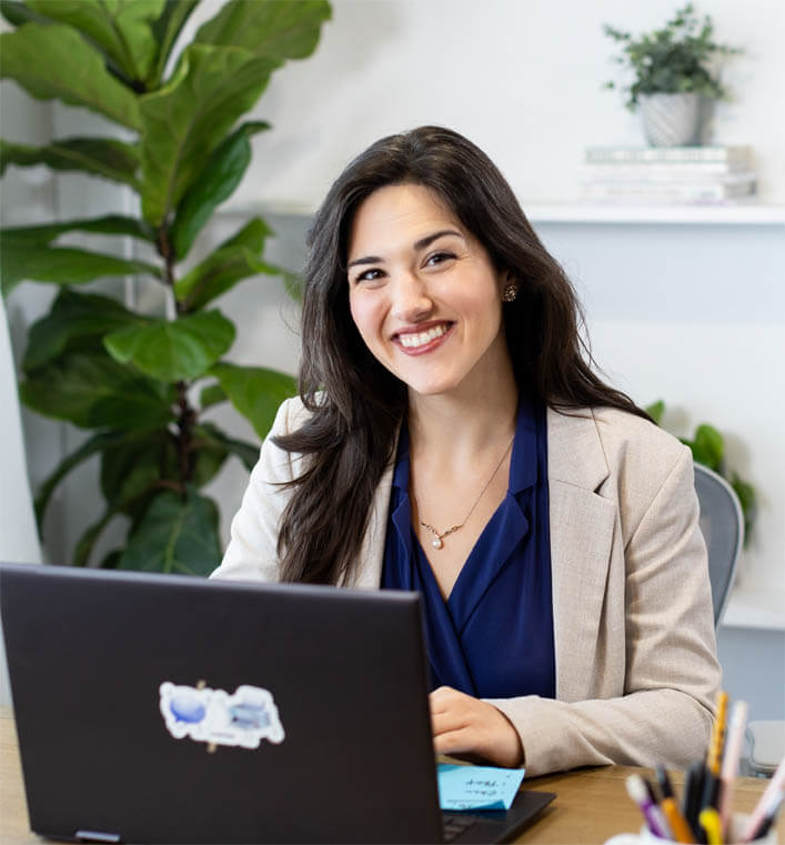 Woman smiles at camera with laptop in front of her as she prepares for a dyslexia therapy appointment