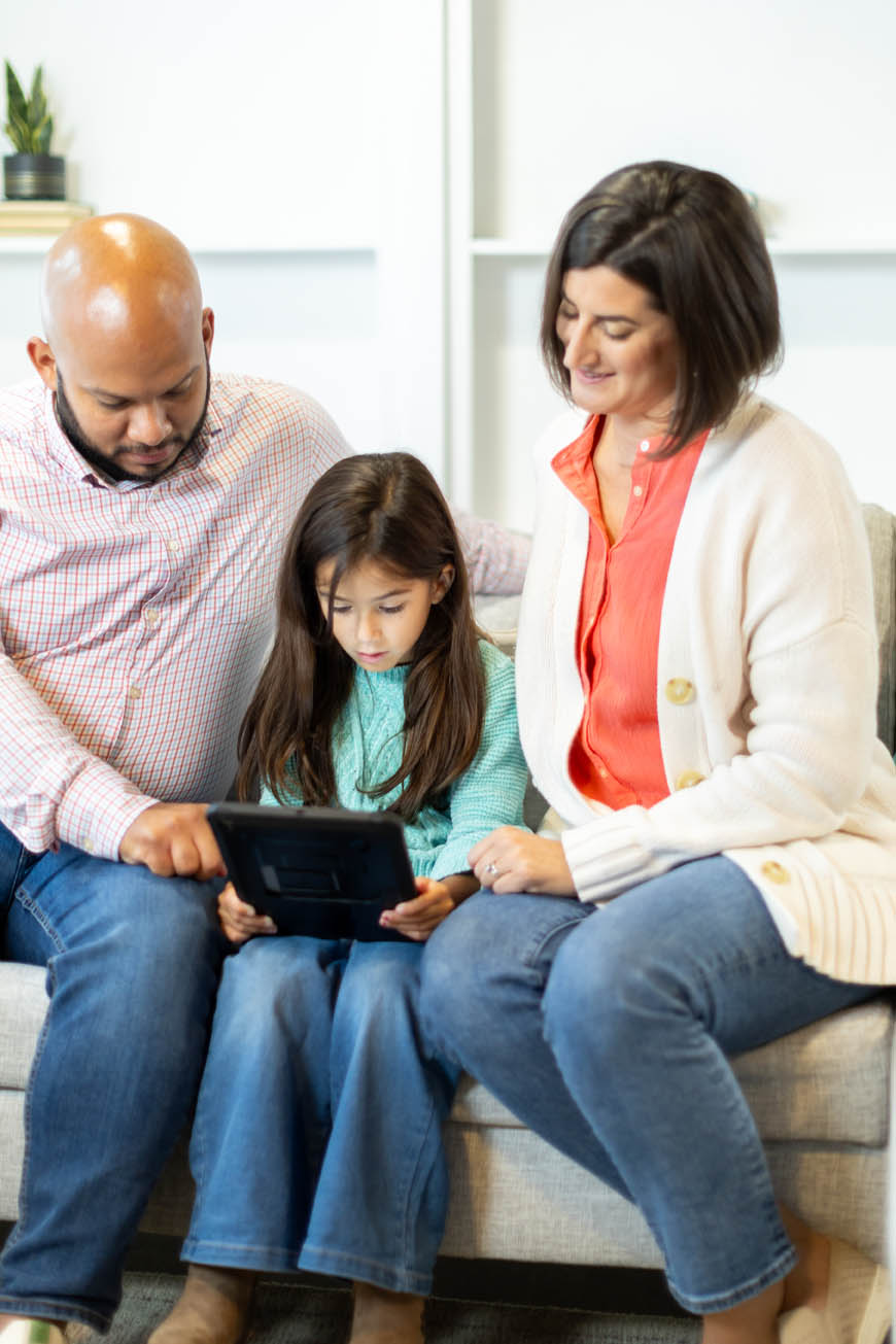 dad, mom, and girl sitting on a couch while girl plays Lexercise educational games on her ipad
